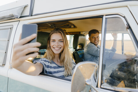 Porträt einer glücklichen Frau, die ein Selfie in einem Wohnmobil mit einem Mann am Steuer macht, lizenzfreies Stockfoto