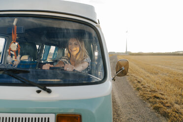 Happy young woman driving camper van in rural landscape - GUSF01431