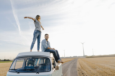 Glückliches Paar auf dem Dach eines Wohnmobils in ländlicher Landschaft - GUSF01436