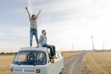 Glückliches Paar auf dem Dach eines Wohnmobils in ländlicher Landschaft - GUSF01437