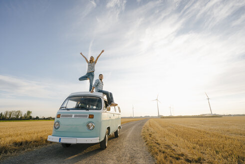 Young couple on roof of a camper van in rural landscape - GUSF01440