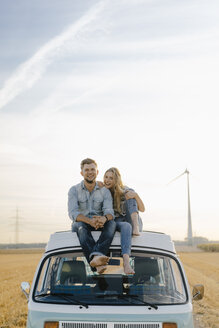 Porträt eines glücklichen jungen Paares auf dem Dach eines Wohnmobils in einer ländlichen Landschaft - GUSF01446