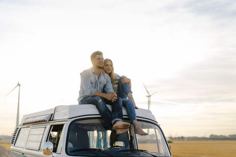 Lächelndes junges Paar auf dem Dach eines Wohnmobils in ländlicher Landschaft, lizenzfreies Stockfoto