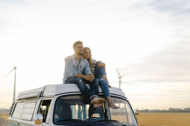 Smiling young couple on roof of a camper van in rural landscape - GUSF01447
