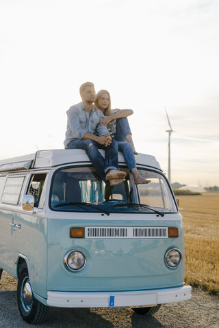 Affectionate young couple on roof of a camper van in rural landscape stock photo