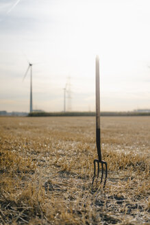 Heugabel auf einem Feld in ländlicher Landschaft mit Windrädern im Hintergrund - GUSF01449