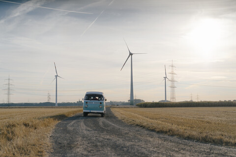 Wohnmobil in ländlicher Landschaft mit Windrädern bei Sonnenuntergang, lizenzfreies Stockfoto