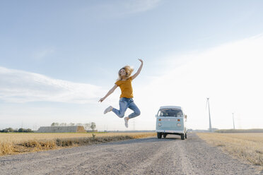 Übermütige junge Frau springt auf Feldweg an Wohnmobil in ländlicher Landschaft - GUSF01451