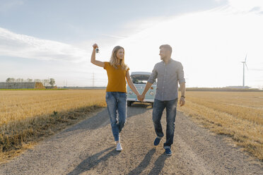 Young couple with car key walking on dirt track at camper van in rural landscape - GUSF01455