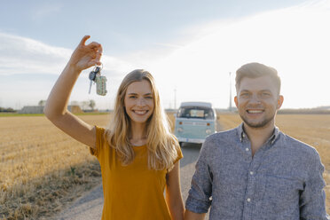 Porträt eines glücklichen jungen Paares mit Autoschlüssel auf unbefestigtem Weg am Wohnmobil in ländlicher Landschaft - GUSF01457