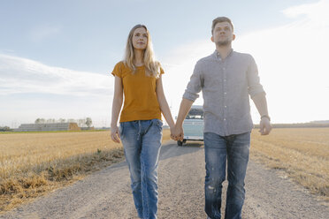 Young couple walking on dirt track at camper van in rural landscape - GUSF01459