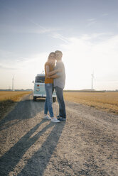Zärtliches junges Paar, das auf einem Feldweg vor einem Wohnmobil in einer ländlichen Landschaft steht - GUSF01465