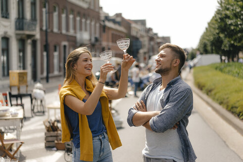 Belgien, Tongeren, glückliches junges Paar mit Gläsern auf einem Antiquitätenflohmarkt - GUSF01484