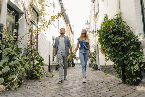 Netherlands, Maastricht, young couple walking hand in hand in an alley - GUSF01495