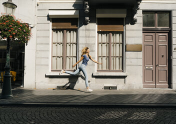 Netherlands, Maastricht, blond young woman running along building in the city - GUSF01514