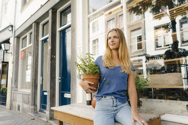 Netherlands, Maastricht, blond young woman holding flowerpot in the city - GUSF01516