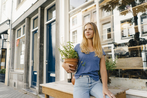 Niederlande, Maastricht, blonde junge Frau mit Blumentopf in der Stadt - GUSF01516