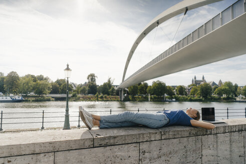 Niederlande, Maastricht, junge Frau liegt auf einer Mauer am Flussufer - GUSF01528