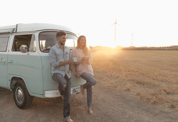 Happy young couple standing at camper van in rural landscape at sunset - GUSF01538