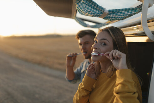 Couple brushing teeth at camper van in rural landscape at sunset - GUSF01542