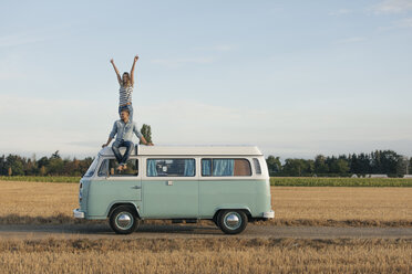 Happy couple on roof of a camper van in rural landscape - GUSF01550