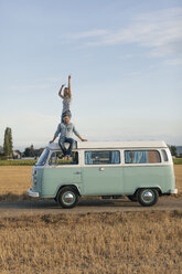 Happy couple on roof of a camper van in rural landscape - GUSF01551