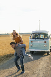 Playful young couple at camper van in rural landscape - GUSF01564
