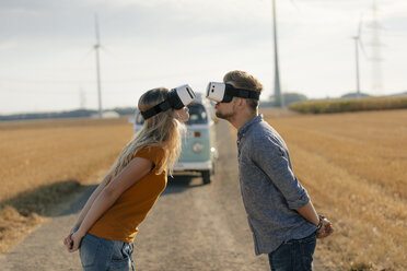 Young couple wearing VR glasses kissing at camper van in rural landscape - GUSF01569