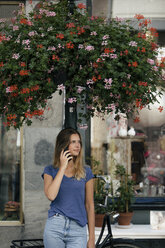 Niederlande, Maastricht, junge Frau telefoniert mit Handy an einem Laternenmast in der Stadt - GUSF01599