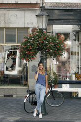Netherlands, Maastricht, smiling young woman on cell phone at lamp pole in the city - GUSF01600