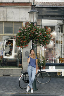 Niederlande, Maastricht, lächelnde junge Frau am Handy an einem Laternenmast in der Stadt - GUSF01600