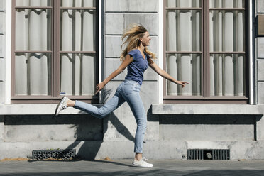 Netherlands, Maastricht, happy blond young woman running along building in the city - GUSF01601