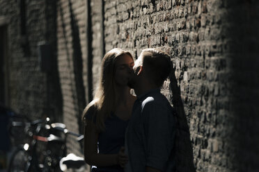 Affectionate young couple kissing at brick wall - GUSF01604