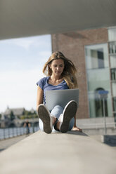 Niederlande, Maastricht, junge Frau sitzt auf einer Mauer am Flussufer und benutzt einen Laptop - GUSF01611