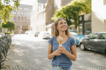 Niederlande, Maastricht, lächelnde blonde junge Frau mit Eiswaffel in der Hand in der Stadt - GUSF01619