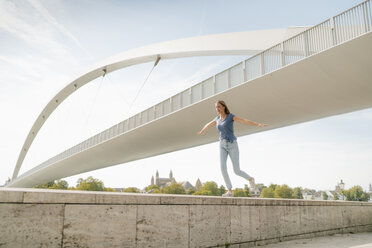 Niederlande, Maastricht, junge Frau balanciert auf einer Mauer an einer Brücke - GUSF01621