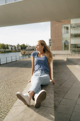 Netherlands, Maastricht, young woman sitting on a wall at the riverside - GUSF01623