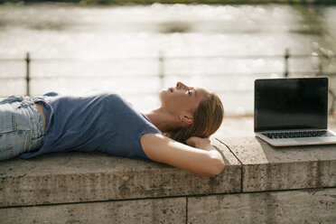 Junge Frau liegt an einer Wand neben einem Laptop - GUSF01624