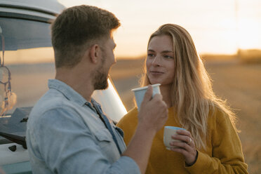 Smiling young couple holding mugs at camper van in rural landscape - GUSF01632