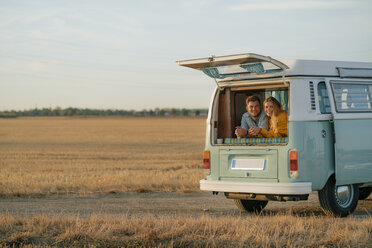 Happy young couple lying in camper van in rural landscape - GUSF01636