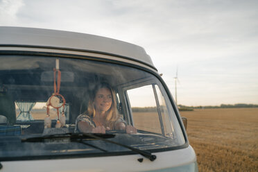 Smiling young woman driving camper van in rural landscape - GUSF01639