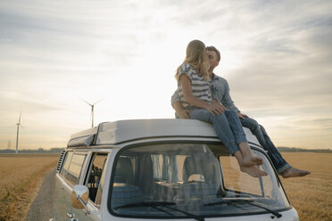 Couple kissing on roof of a camper van in rural landscape - GUSF01646