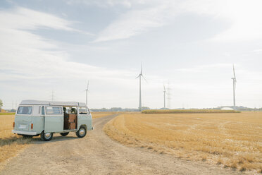 Camper van parked on dirt track in rural landscape with wind turbines - GUSF01653