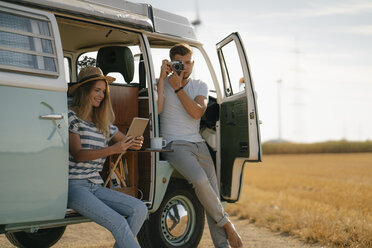 Young couple with tablet and camera at camper van in rural landscape - GUSF01657