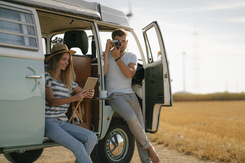 Junges Paar mit Tablet und Kamera am Wohnmobil in ländlicher Landschaft - GUSF01657