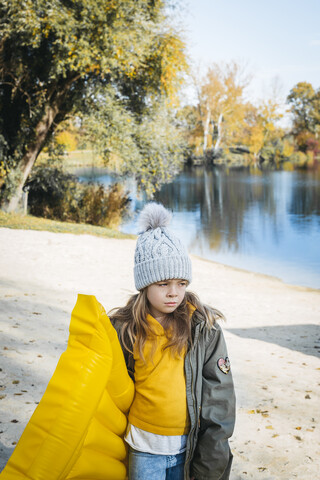 Porträt eines Mädchens mit gelber Luftmatratze am Strand im Herbst, lizenzfreies Stockfoto