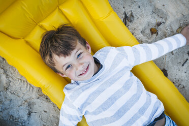 Porträt eines lächelnden kleinen Jungen auf einer gelben Luftmatratze am Strand im Herbst - HMEF00080