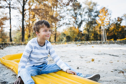 Content little boy sitting on yellow airbed on the beach in autumn - HMEF00084