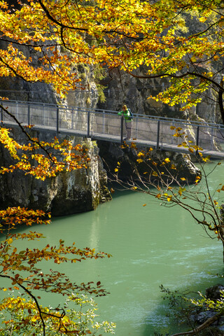 Österreich, Tirol, Wanderer auf Hängebrücke mit Blick auf die Tiroler Ache im Herbst, lizenzfreies Stockfoto