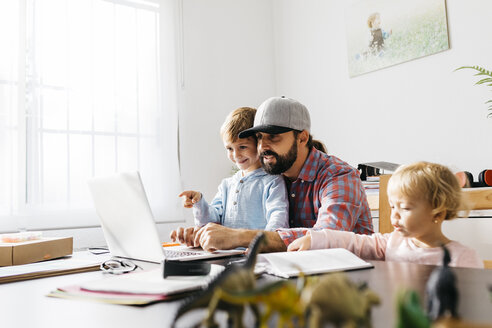 Father working at home, using laptop with his children on his lap - JRFF01983